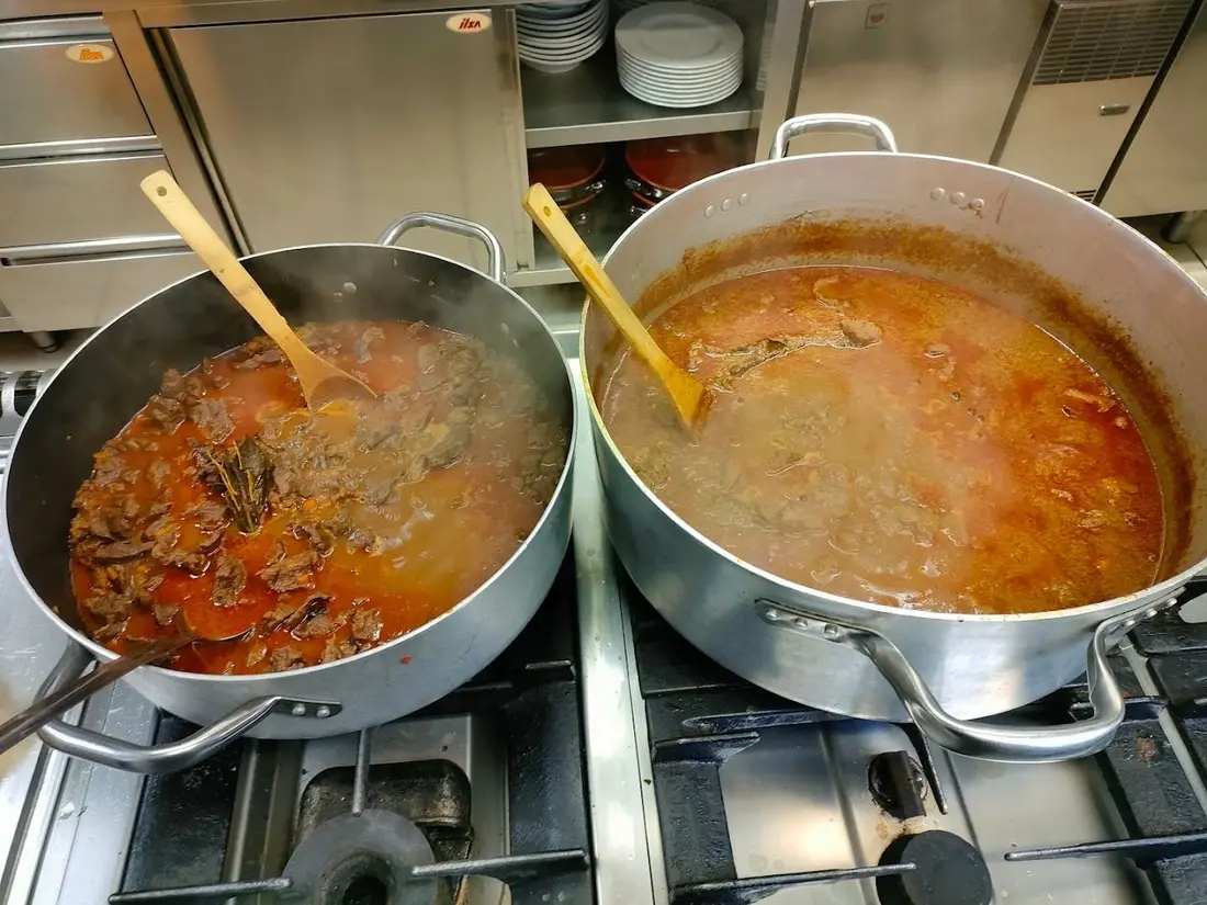 Due grandi pentole di umido sul fuoco nella cucina del ristorante, con i mestoli di legno