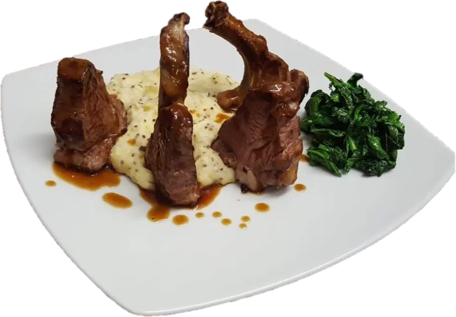 Piatto bianco con costolette su un purè, spinaci e gocce di riduzione