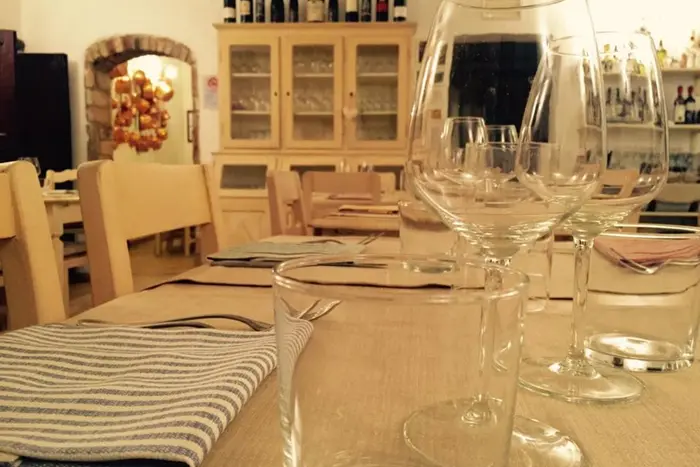 La sala: tavoli apparecchiati con bicchieri da vino, una credenza color crema e un arco di mattoni